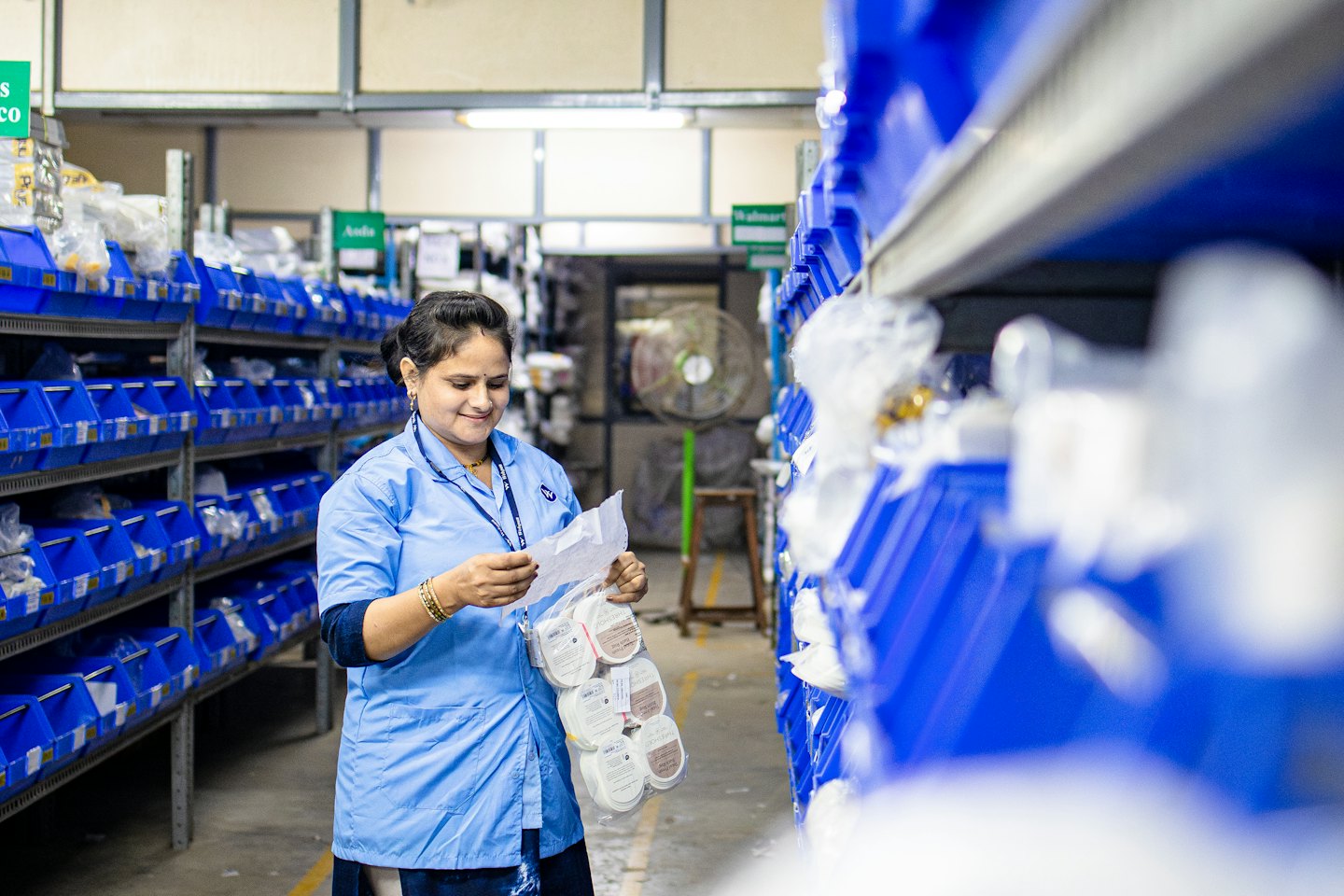 Woman checks inventory in a warehouse among storage bins.